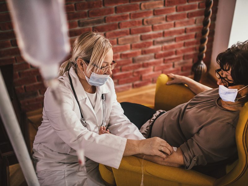 A masked healthcare professional attending to a patient lying on a couch.