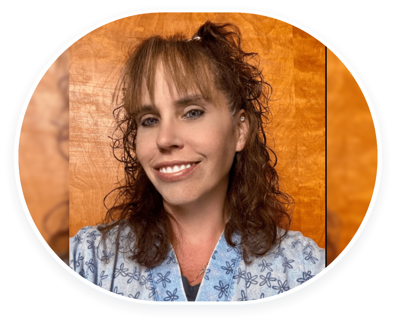 Smiling woman with curly hair and bangs in a blue patterned shirt.